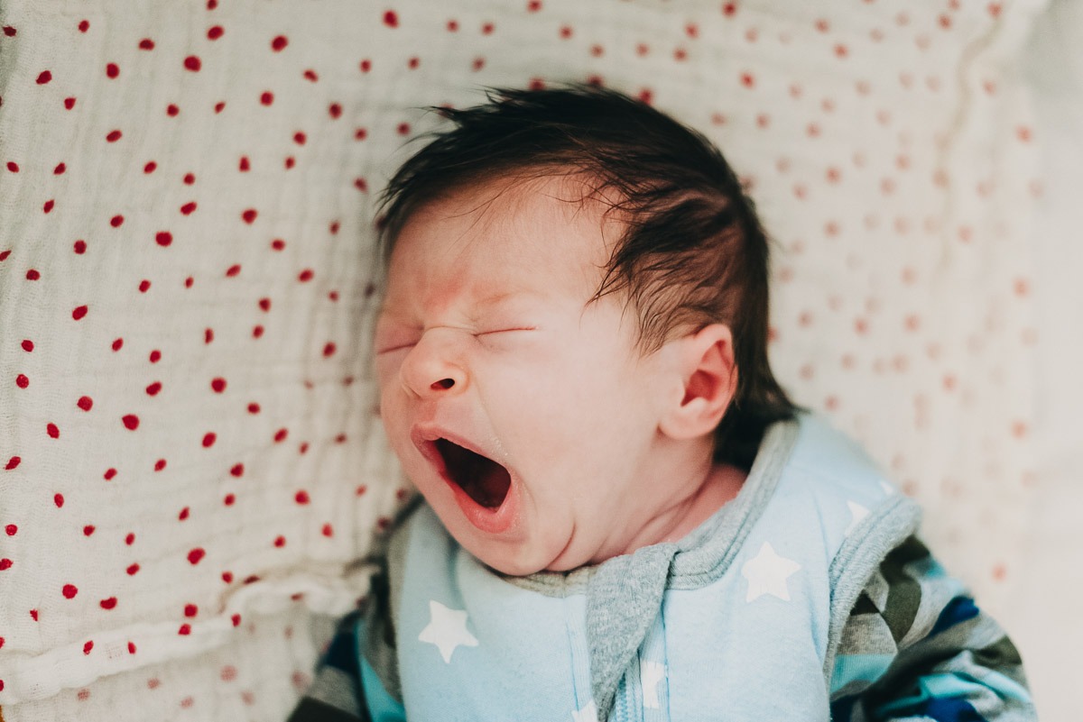 Ein Neugeborenes liegt in seinem Bett und gähnt ausgiebig.