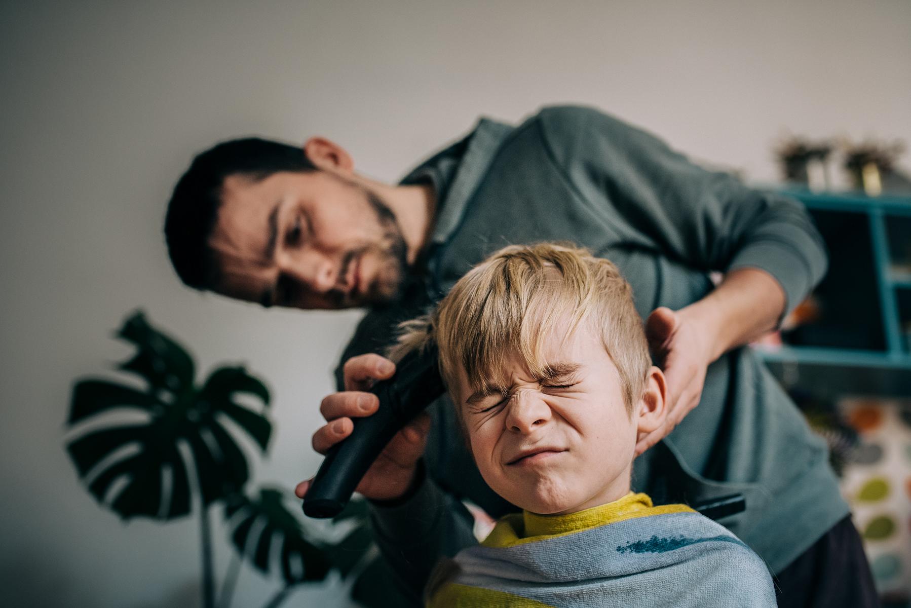 Ein Vater schneidet seinem Sohn mit einer Maschine die Haare.