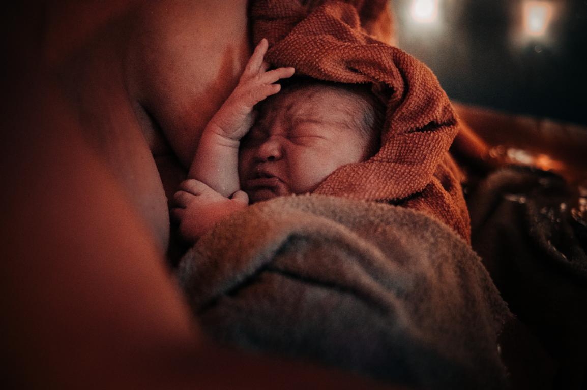 Ein frischgeborenes Baby, in Tücher gehüllt, an der Brust der Mutter.