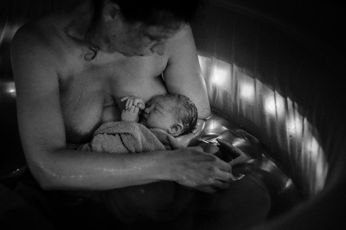 Intime Schwarz-Weiß-Aufnahme einer Mutter, die ihr frischgeborenes Kind im Arm hält.