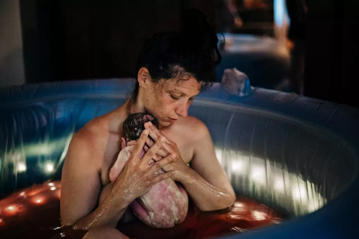 Eine Mutter im Geburtspool drückt ihr Baby an sich.