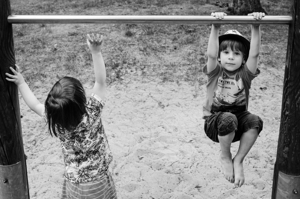 Schwarz-weißes Familienfoto von zwei Kindern, die auf dem Spielplatz spielen.